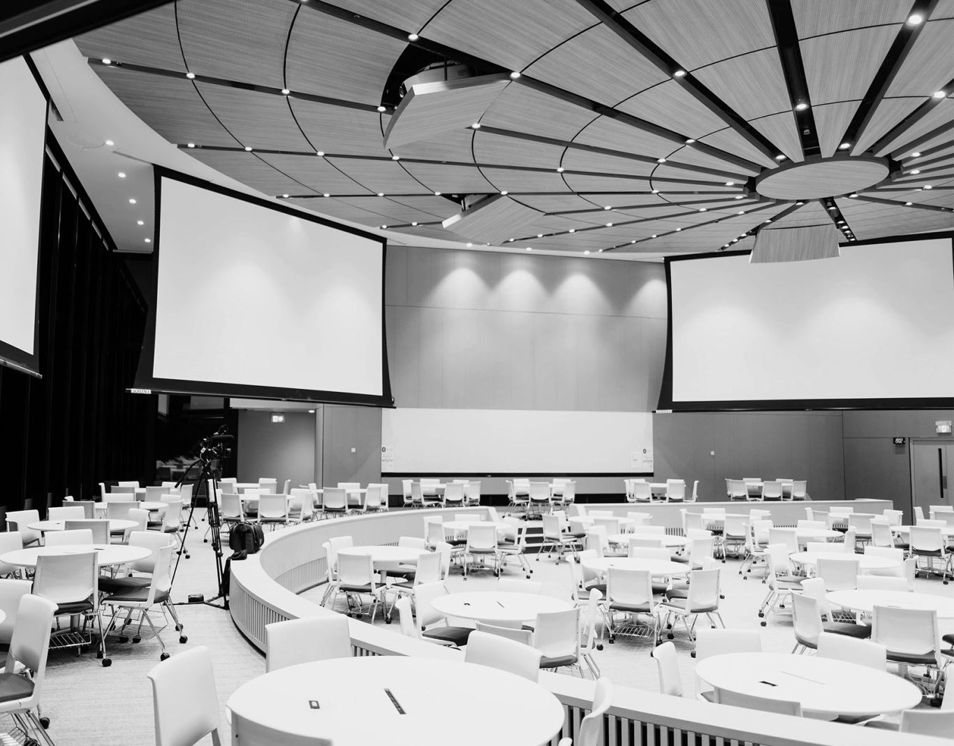 Zielgruppe Rundsaal mit Tischen und Stuhlreihen, Leinwände an der Decke montiert.